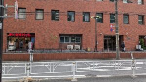 マインズタワー脇の通路を出ると、ニューステートメナーの向かい側です。まいばすけっとの右側にあるガラス扉が玄関です。